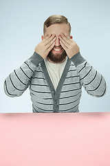 Image showing Young man sitting at table at studio with eyes closed isolated on blue