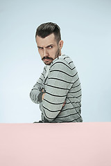 Image showing Serious suspicious business man sitting at a table on a blue background