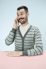 Image showing Smiling happy business man talking on phone sitting at the table