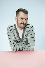 Image showing Serious suspicious business man sitting at a table on a blue background