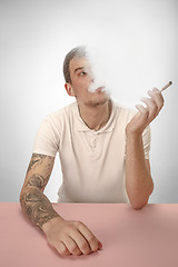 Image showing Handsome hipster man smoking cigarette at home. Man looking upwards and enjoying spending free time.