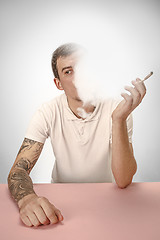 Image showing Handsome hipster man smoking cigarette at home. Man looking upwards and enjoying spending free time.