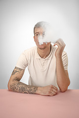 Image showing Handsome hipster man smoking cigarette at home. Man looking upwards and enjoying spending free time.