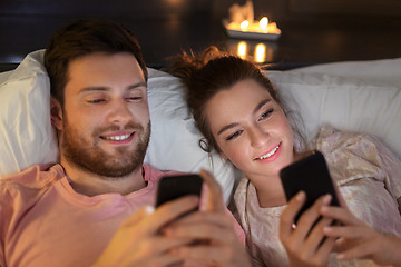 Image showing happy couple using smartphones in bed at night