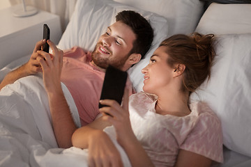 Image showing happy couple using smartphones in bed at night