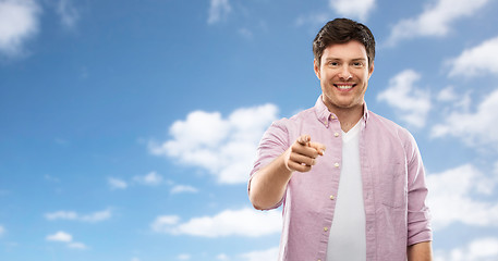 Image showing smiling man pointing fingers at you over sky