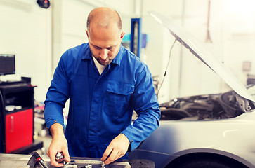 Image showing mechanic man with wrench repairing car at workshop