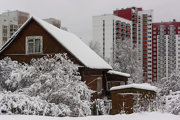 Image showing Old wooden house against the background of new tall city houses in winter