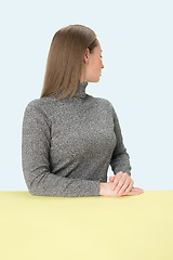 Image showing Serious business woman sitting at a table on a pink background