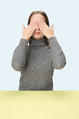 Image showing Young woman sitting at table at studio with eyes closed isolated on blue