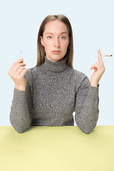 Image showing Handsome young women smoking while sitting at table at studio. Trendy colors