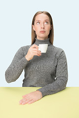 Image showing Beautiful lonely woman sitting at studio and looking sad holding the cup of coffee in hand. Closeup toned portrait