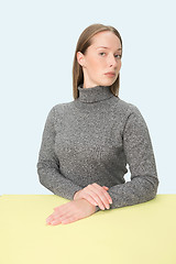 Image showing Serious business woman sitting at a table on a pink background