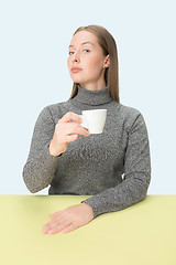 Image showing Beautiful lonely woman sitting at studio and looking sad holding the cup of coffee in hand. Closeup toned portrait