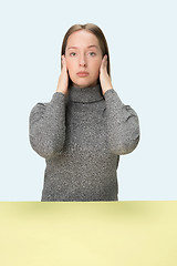 Image showing portrait of stressed woman sitting at table with closed and covering her ears with hands.