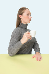 Image showing Beautiful lonely woman sitting at studio and looking sad holding the cup of coffee in hand. Closeup toned portrait