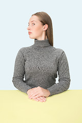 Image showing Serious business woman sitting at a table on a pink background