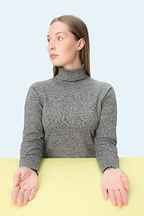 Image showing Serious business woman sitting at a table on a pink background