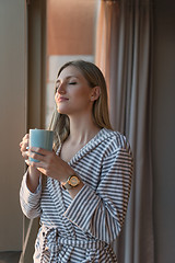 Image showing young woman enjoying evening coffee by the window