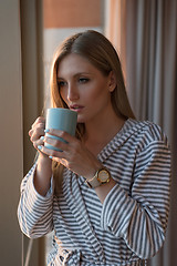 Image showing young woman enjoying evening coffee by the window