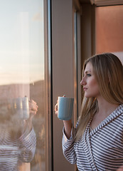 Image showing young woman enjoying evening coffee by the window