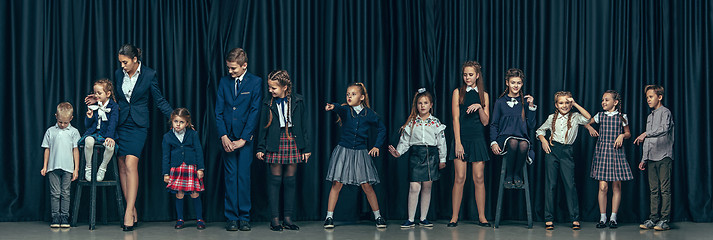 Image showing Cute stylish children on dark studio background. The beautiful teen girls and boy standing together