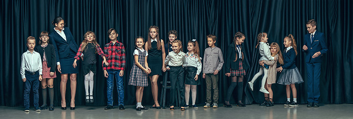 Image showing Cute stylish children on dark studio background. The beautiful teen girls and boy standing together