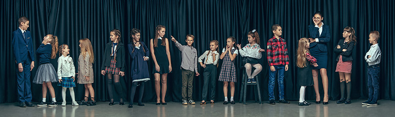 Image showing Cute stylish children on dark studio background. The beautiful teen girls and boy standing together