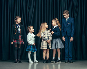 Image showing Cute stylish children on dark studio background. The beautiful teen girls and boy standing together