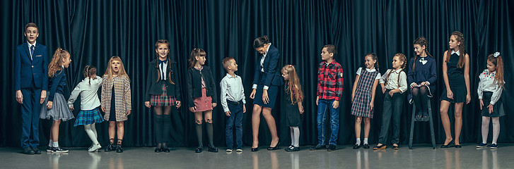 Image showing Cute stylish children on dark studio background. The beautiful teen girls and boy standing together