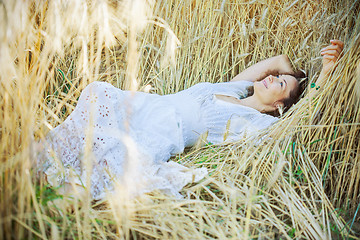 Image showing beautiful woman in a white dress lies in the ears of corn