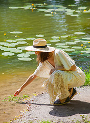 Image showing Beautiful woman in a white dress and straw hat on the shore of a