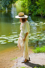 Image showing woman in a straw hat and white summer dress on the shore of an o