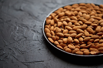 Image showing Whole almond nuts in black plate placed on black stone table