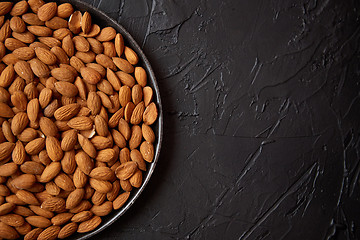 Image showing Whole almond nuts in black plate placed on black stone table