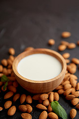 Image showing Fresh almond milk in wooden bowl and almonds on black stone background