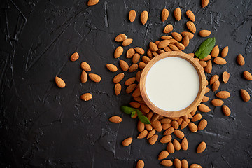 Image showing Fresh almond milk in wooden bowl and almonds on black stone background