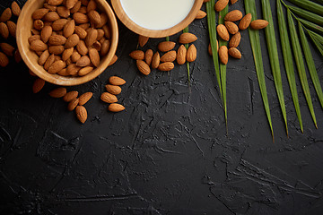 Image showing Amond seeds in wooden bowl, fresh natural milk placed on black stone background