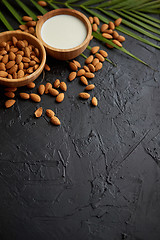 Image showing Amond seeds in wooden bowl, fresh natural milk placed on black stone background