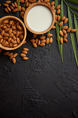 Image showing Amond seeds in wooden bowl, fresh natural milk placed on black stone background