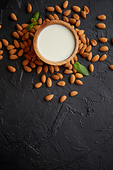 Image showing Fresh almond milk in wooden bowl and almonds on black stone background