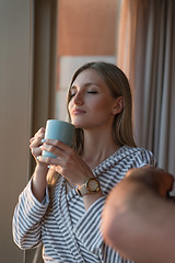 Image showing young woman enjoying evening coffee by the window