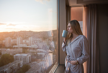 Image showing young woman enjoying evening coffee by the window