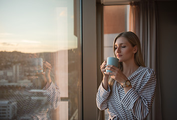 Image showing young woman enjoying evening coffee by the window