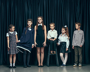 Image showing Cute stylish children on dark studio background. The beautiful teen girls and boy standing together