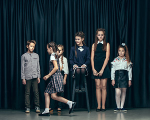 Image showing Cute stylish children on dark studio background. The beautiful teen girls and boy standing together