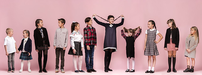 Image showing Cute stylish children on pink studio background. The beautiful teen girls and boy standing together