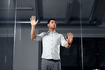 Image showing businessman touching glass wall at night office