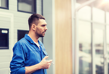 Image showing auto mechanic smoking cigarette at car workshop