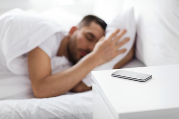 Image showing smartphone on bedside table near sleeping man